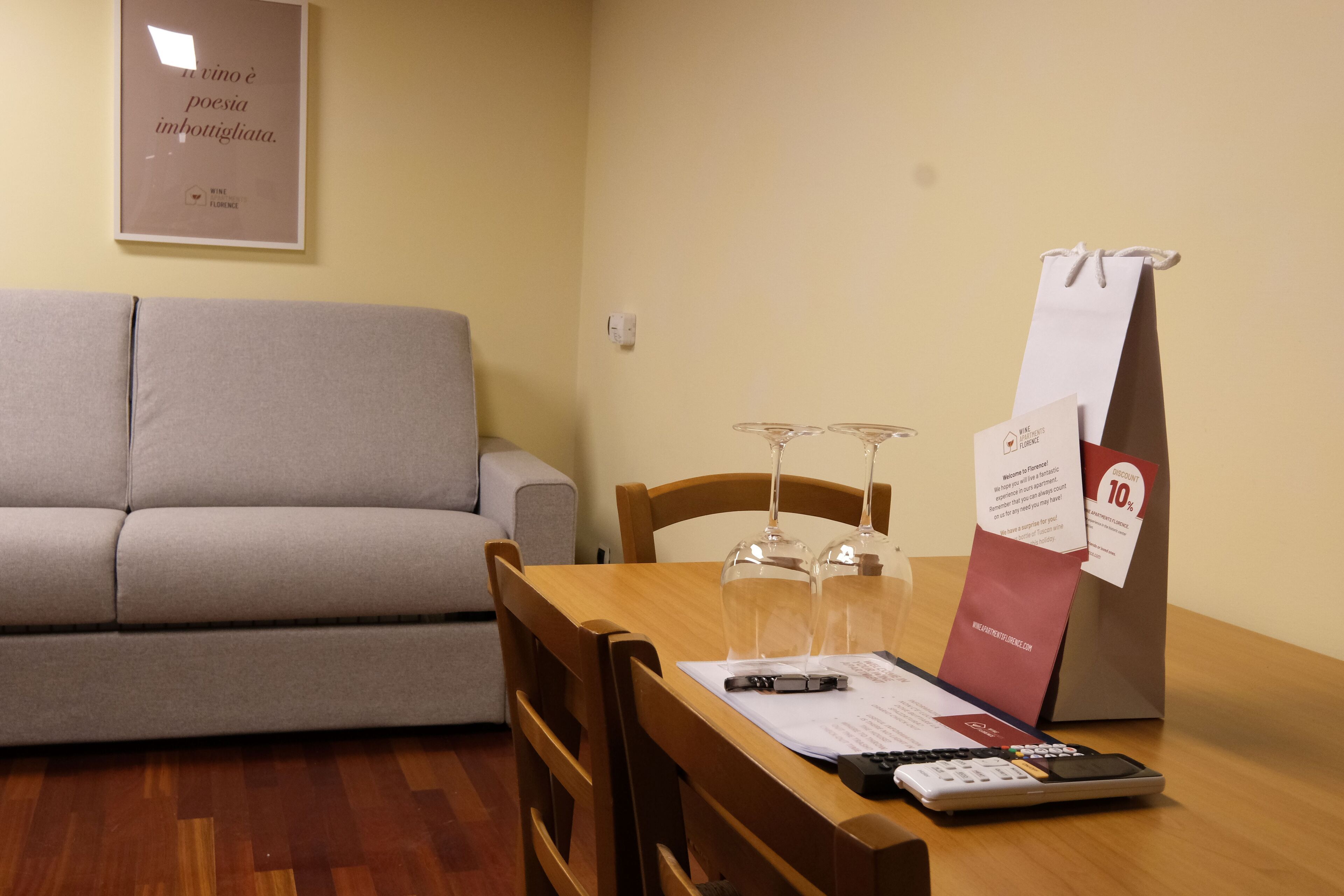 Un comedor con una mesa de madera, sillas, un menú, una copa de vino y una bolsa con material promocional.