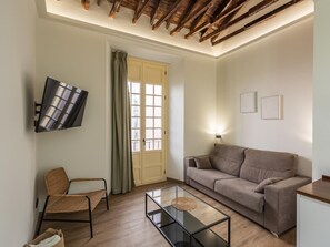 Una sala de estar con sofá, sillón, televisión montada en la pared y ventana con cortinas.
