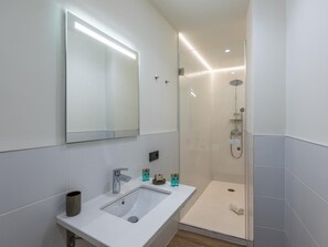 Un baño moderno con un espejo grande, un lavamanos y una ducha a pie.