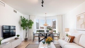 A modern living room with a flat-screen TV, a dining table with chairs, a sofa, and a large window with curtains. - Avenida Andalucía - iloftmalaga (Málaga)