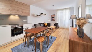 Eine moderne Küche mit Holzausstattung, ein Essbereich mit Holztisch und -stühlen sowie ein Wohnbereich mit Sofa und Lampe.