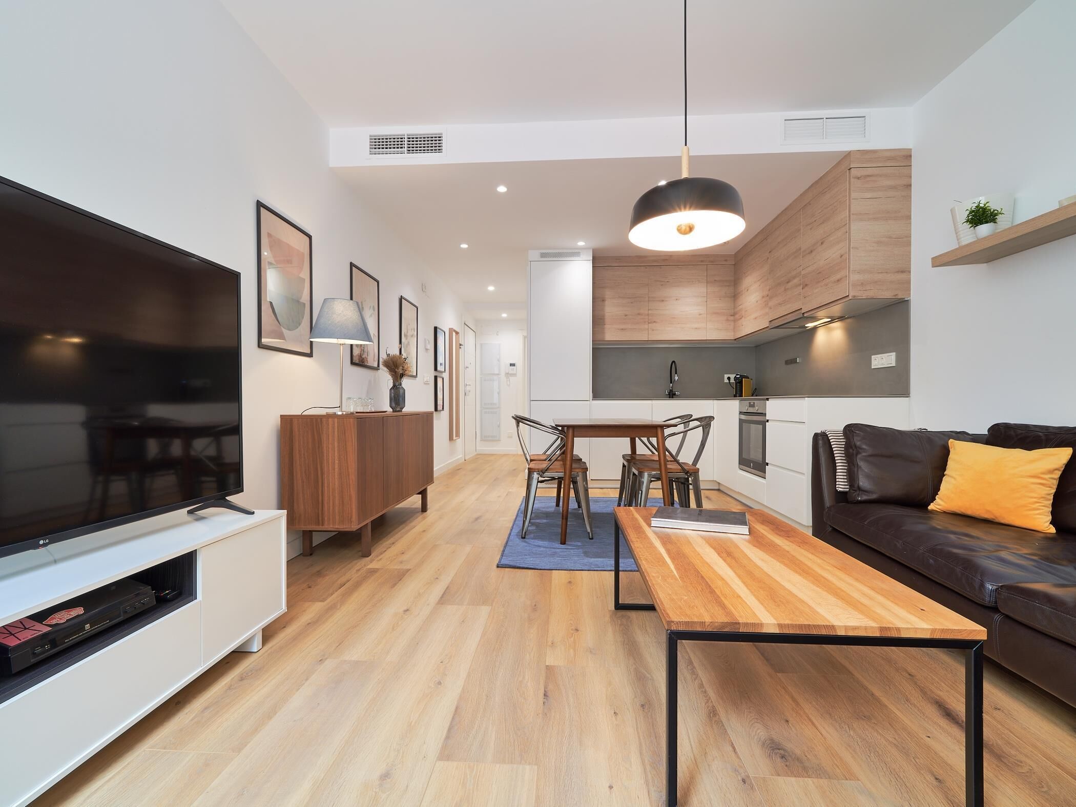 Una sala de estar moderna con un televisor de pantalla plana, muebles de madera y un comedor con mesa y sillas.