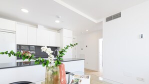 Une cuisine moderne avec des meubles blancs, un îlot central en verre et un coin repas comprenant une table et des chaises en verre.
