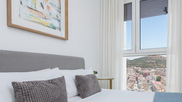 Une chambre avec un grand lit, une vue sur la ville, un tableau au mur et une fenêtre avec des rideaux.