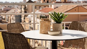 A balcony with wicker chairs, a table, a potted plant, and a woven basket.