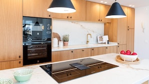 A modern kitchen with wooden cabinets, a built-in oven, a countertop with a sink, and two pendant lights.