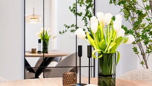 Un intérieur moderne avec une table en bois, un vase de fleurs blanches et un miroir qui reflète la pièce.