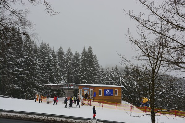 Un petit bâtiment en bois, agrémenté d’une enseigne, entouré d’arbres couverts de neige et situé à proximité d’une piste de ski.