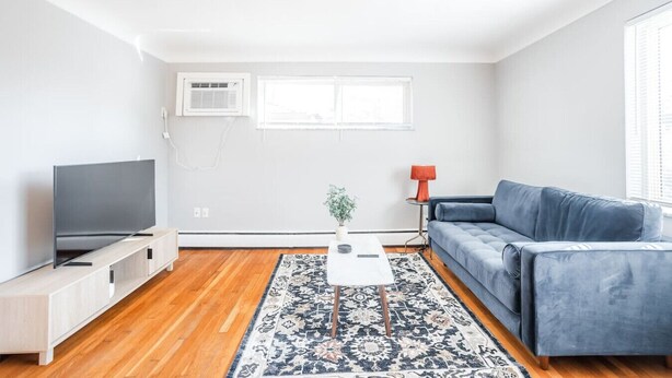 A modern living room with a flat-screen TV, a blue sofa, a coffee table, and a patterned rug.