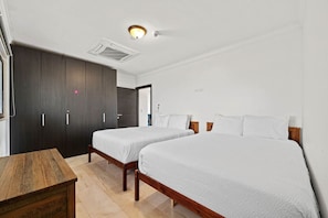 A hotel room with two beds, a wooden table, and a wardrobe. - Noord Paradise! 2BR Condo with Pool and Gym Access (Noord)