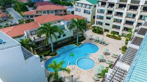 A hotel with a swimming pool, multiple balconies, and a landscaped area with palm trees. - 2BR Condo w/ Pool & Gym, near Palm Beach (Noord)