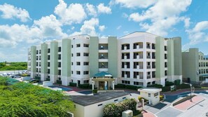 A multi-story hotel with a central courtyard, balconies, and a parking area. - 2BR Condo w/ Pool & Gym, near Palm Beach (Noord)