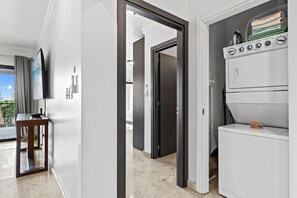 Une chambre d’hôtel dotée d’une grande fenêtre, d’un téléviseur à écran plat, d’une table de chevet en bois et d’une machine à laver.