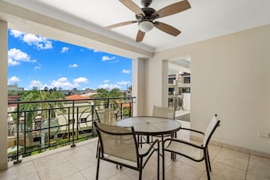 A balcony with a table and chairs, a ceiling fan, and a view of buildings and trees. - Noord Paradise! 2BR Condo with Pool and Gym Access (Noord)