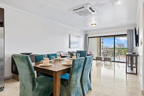 A dining area with a wooden table set for six, surrounded by teal upholstered chairs. - Noord Paradise! 2BR Condo with Pool and Gym Access (Noord)
