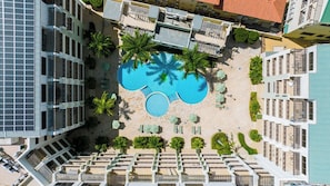 An aerial view of a hotel with a central swimming pool surrounded by palm trees and sun loungers. - Noord Paradise! 2BR Condo with Pool and Gym Access (Noord)