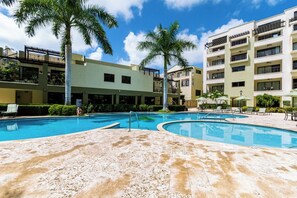 A hotel with a swimming pool, palm trees, and a multi-story building. - 2BR Condo w/ Pool & Gym, near Palm Beach (Noord)