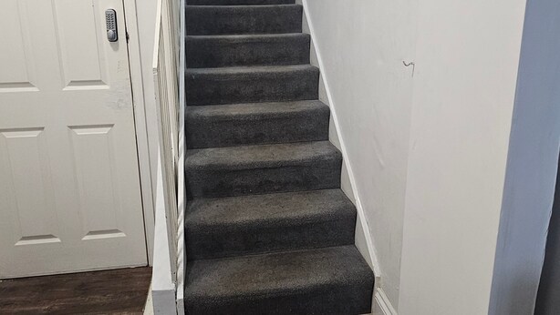 Eine Treppe mit dunkel teppichbesetzten Stufen, die zu einer weißen Tür führt.