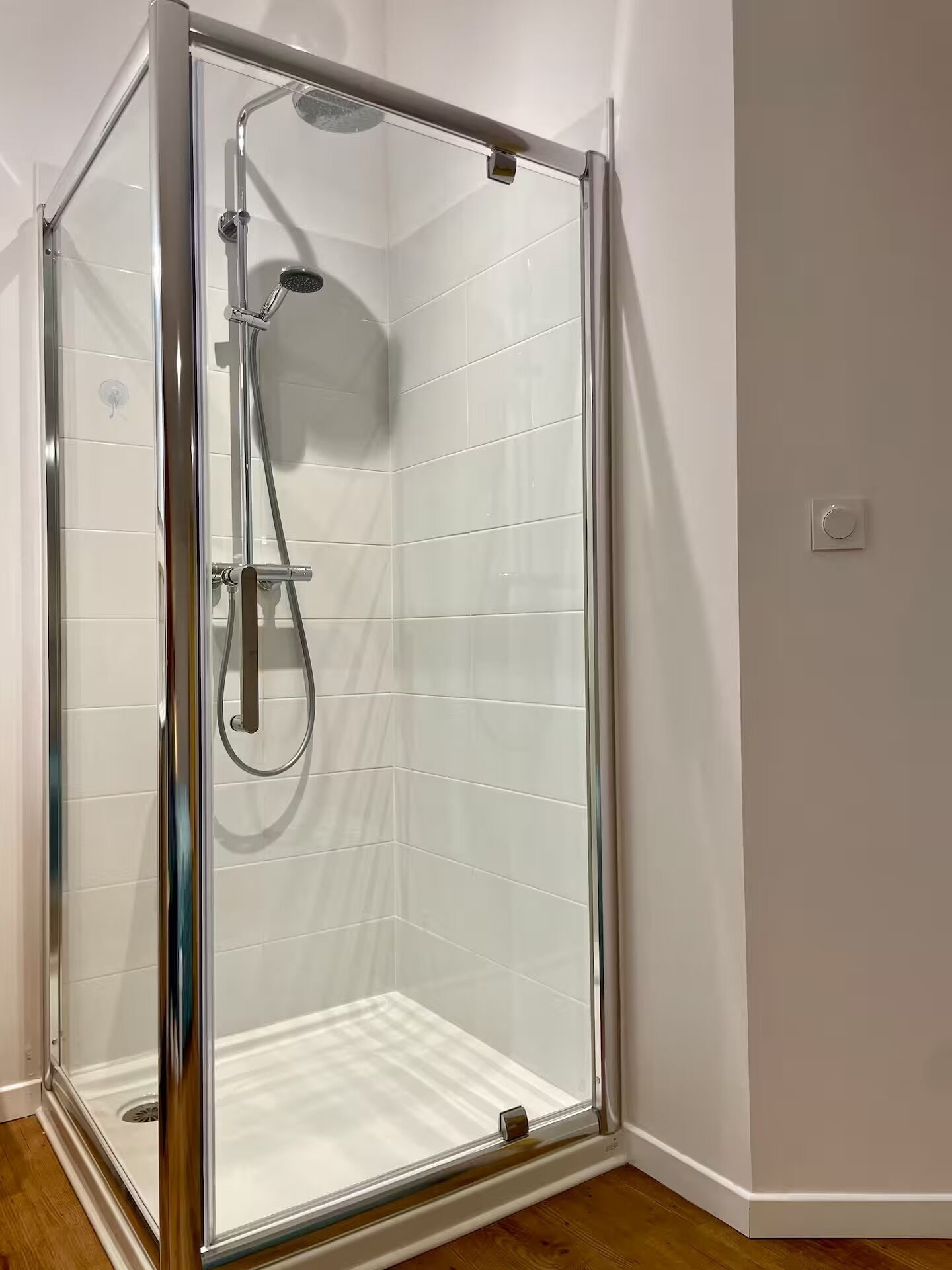 A glass-enclosed shower with a handheld showerhead and a wall-mounted faucet.