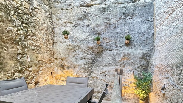Un espacio de estar al aire libre rústico con pared de piedra, mesa de madera y bancos.