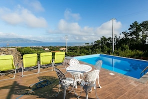 A poolside area with a view of the sea, a table with chairs, and a hose on the ground. - Adegada Quinta- Beautiful Cottage in Madalena (Madalena)