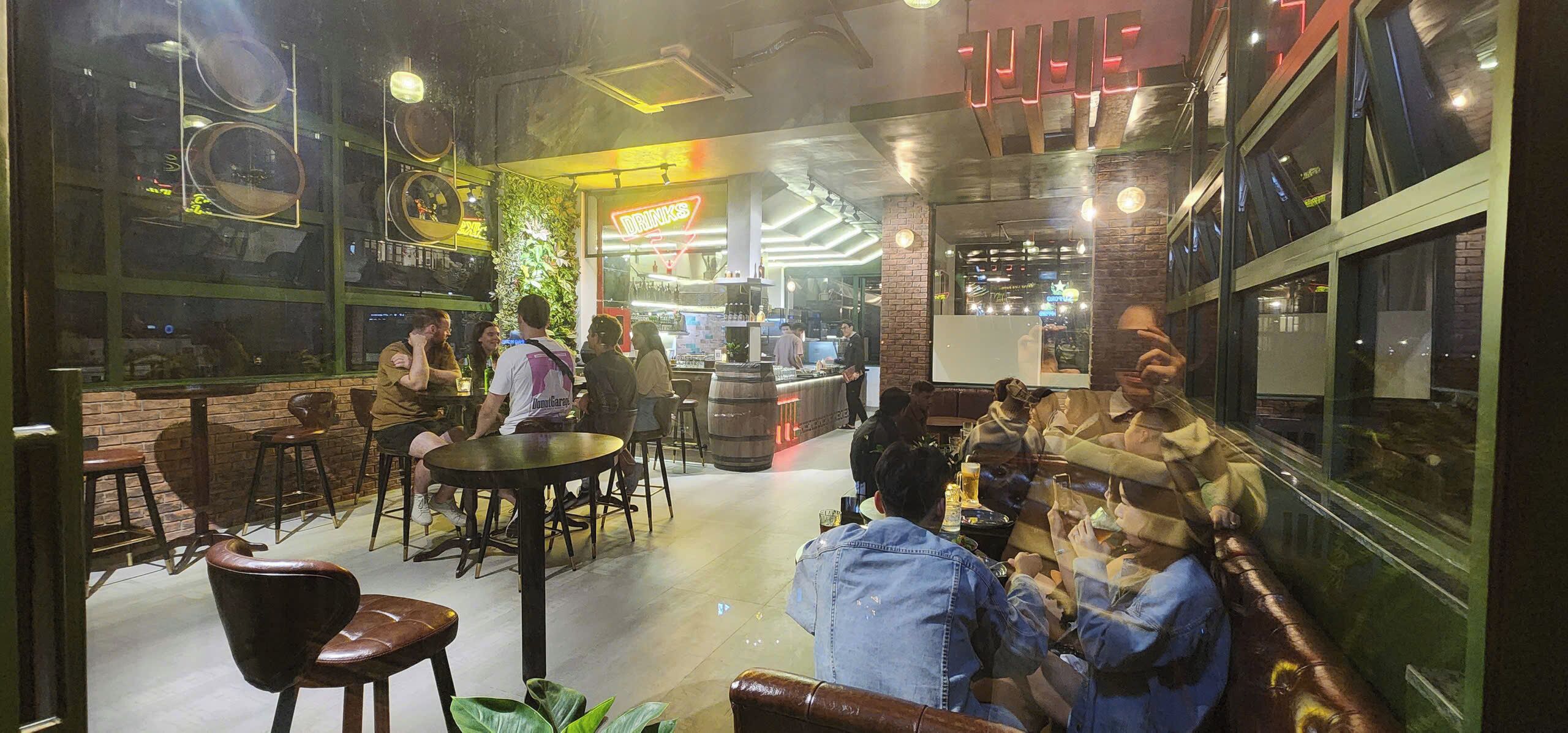 A cozy bar area with round tables, comfortable seating, and a neon sign in the background.