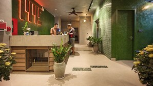 Een receptiegedeelte met een modern design, inclusief een receptiebalie, potplanten en een groene wand met een betegeld patroon.