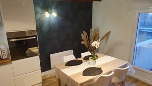 A modern kitchen with a built-in oven, a dining table with chairs, and a decorative vase with pampas grass. - Cosy apartment for curists or tourists (sleeps 2 to 6) (Saujon)