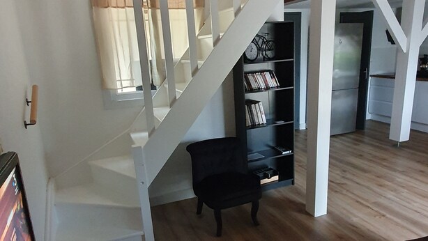 A spacious living area with a staircase, a bookshelf, and a television. - Cosy apartment for curists or tourists (sleeps 2 to 6) (Saujon)