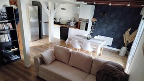 A modern living room with a beige sofa, a dining table with chairs, and a kitchen area with white cabinets and appliances. - Cosy apartment for curists or tourists (sleeps 2 to 6) (Saujon)