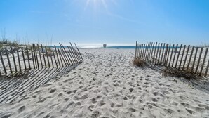 Ein Sandweg am Strand, gesäumt von einem Holzzaun auf beiden Seiten, der zum Meer führt.
