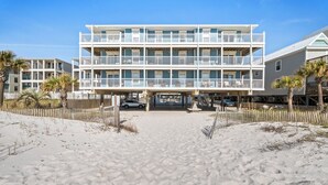 Ein Strandhotel mit mehrstöckiger Bebauung, überdachter Eingang und einem Sandstrand davor.