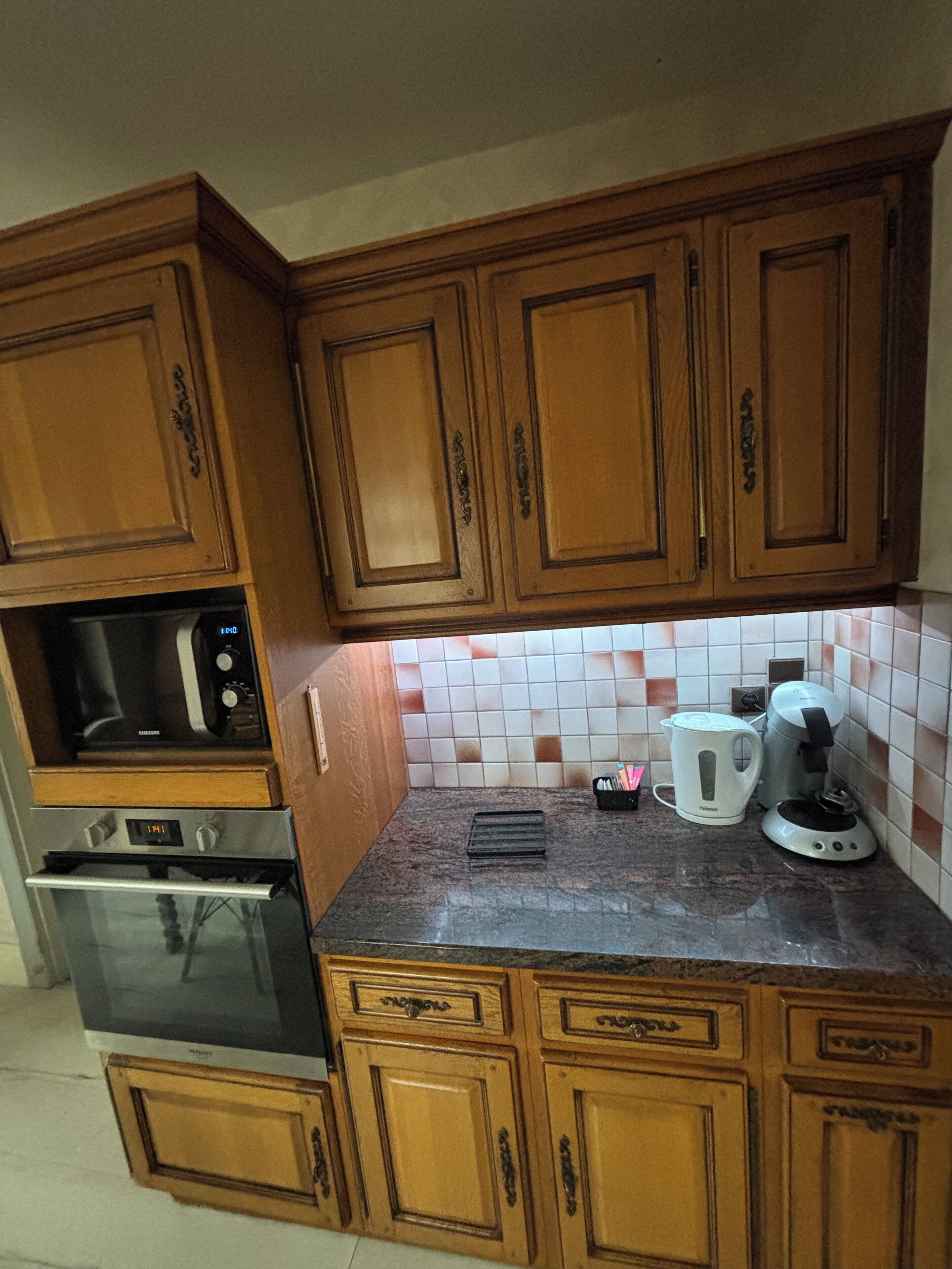 A kitchen with wooden cabinets, a microwave, an oven, a coffee maker, and a kettle.