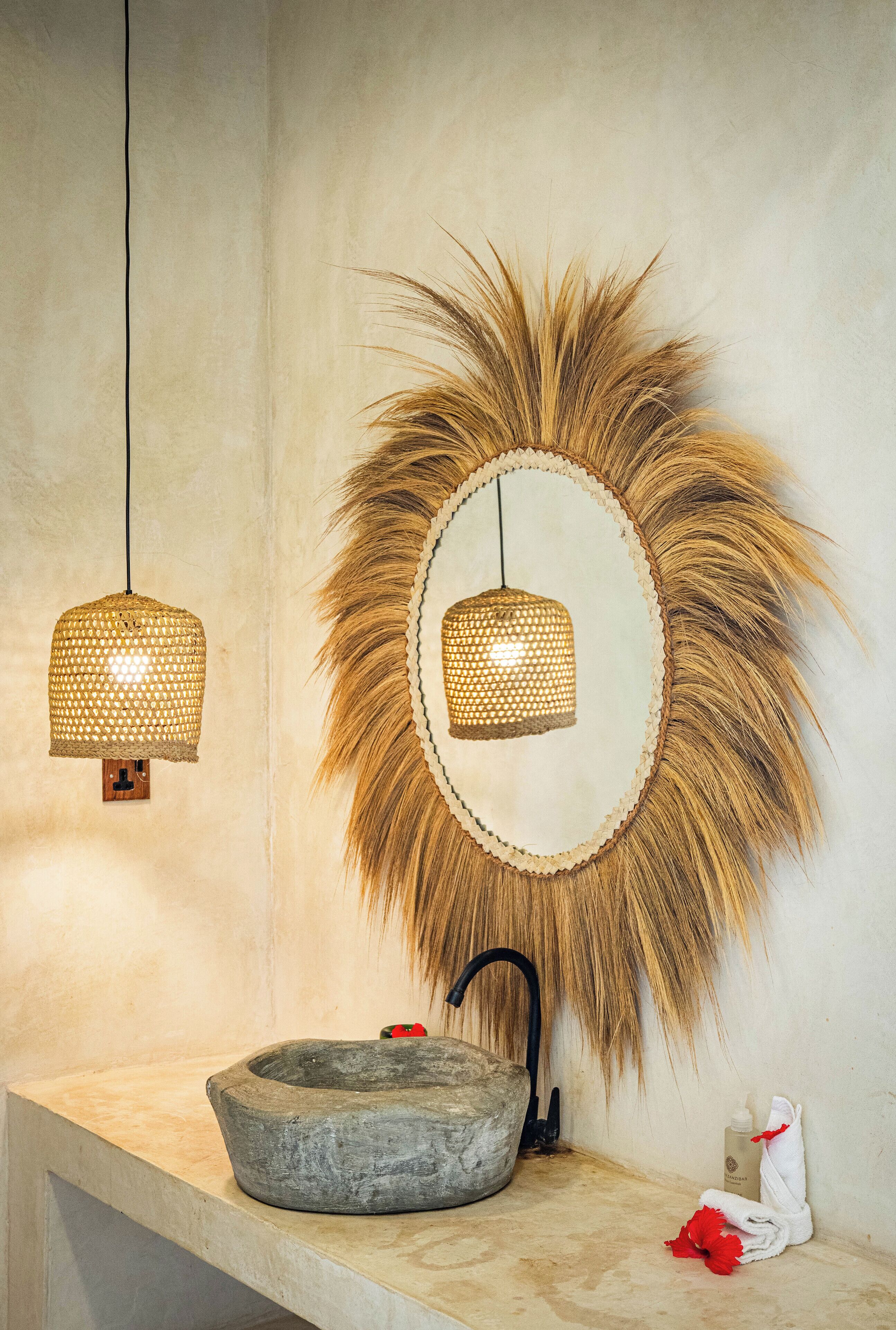 A bathroom with a stone basin, a mirror with a sunburst frame, and two hanging lights.
