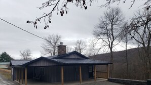 A rustic wooden building with a stone chimney, a covered porch, and a gravel driveway. - LAUREL HIGHLANDS MOUNTAIN RETREAT - Only 7 miles to Ohiopyle! (Confluence)