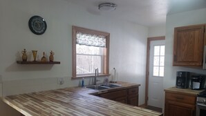 A kitchen with a central island, wooden cabinets, a window with a view, and a coffee maker. - LAUREL HIGHLANDS MOUNTAIN RETREAT - Only 7 miles to Ohiopyle! (Confluence)