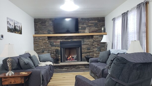 A living room with a stone fireplace, two sofas, a TV mounted above the fireplace, and a window with curtains. - LAUREL HIGHLANDS MOUNTAIN RETREAT - Only 7 miles to Ohiopyle! (Confluence)
