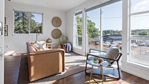 A spacious living room with a large window, a sofa, a chair, and a small table. - Gardenia at Evergreen | A Stylish Flat In Downtown RDD (Redding)