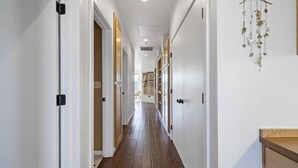 A hallway with wooden flooring, white walls, and doors leading to rooms. - Gardenia at Evergreen | A Stylish Flat In Downtown RDD (Redding)