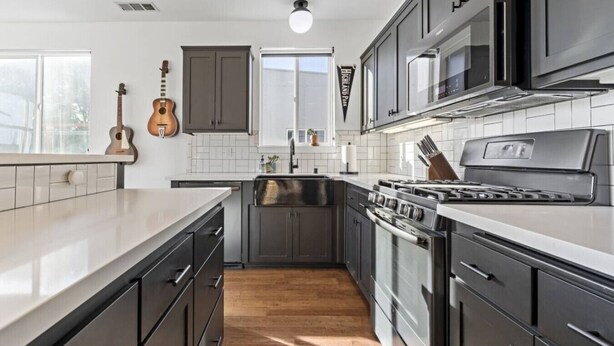 A modern kitchen with dark cabinetry, a stainless steel stove, and a wooden floor. - Pine at Evergreen - Boutique Hotel (Redding)