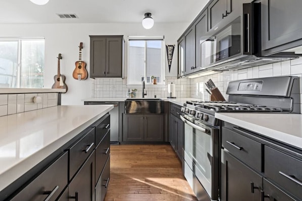 A modern kitchen with dark cabinetry, a stainless steel stove, and a wooden floor.