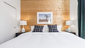 A hotel room with a wooden headboard, a framed picture, two bedside lamps, and a bed with white bedding. - Pine at Evergreen - Boutique Hotel (Redding)