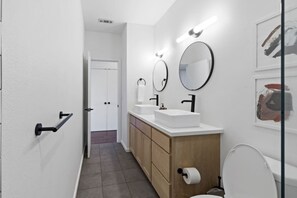 Ein modernes Badezimmer mit einem weißen Waschbecken, zwei Spiegeln, einer Toilette und einem Holzschrank.