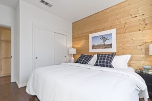 Ein Schlafzimmer mit einem hölzernen Kopfende, einem Bett mit weißer Bettwäsche, einem Nachttisch mit einer Lampe und einem gerahmten Bild an der Wand.