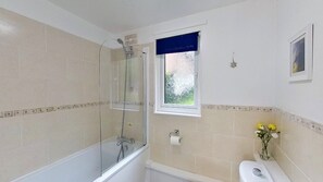 Une salle de bain dotée d’une douche à parois de verre, d’une baignoire, de toilettes et d’une fenêtre donnant sur un espace verdoyant.