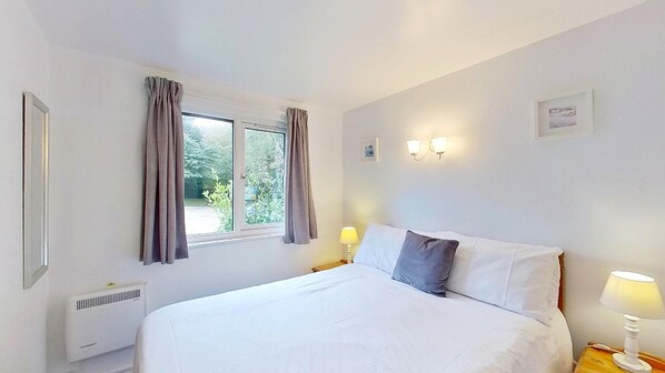 Une chambre à coucher comprenant un lit, deux lampes de chevet, une fenêtre avec des rideaux, un luminaire fixé au mur et un radiateur.