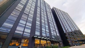 Un edificio moderno con fachada de vidrio, una entrada visible con la leyenda "ENTRADA S-01" y una escalera que conduce a la entrada.