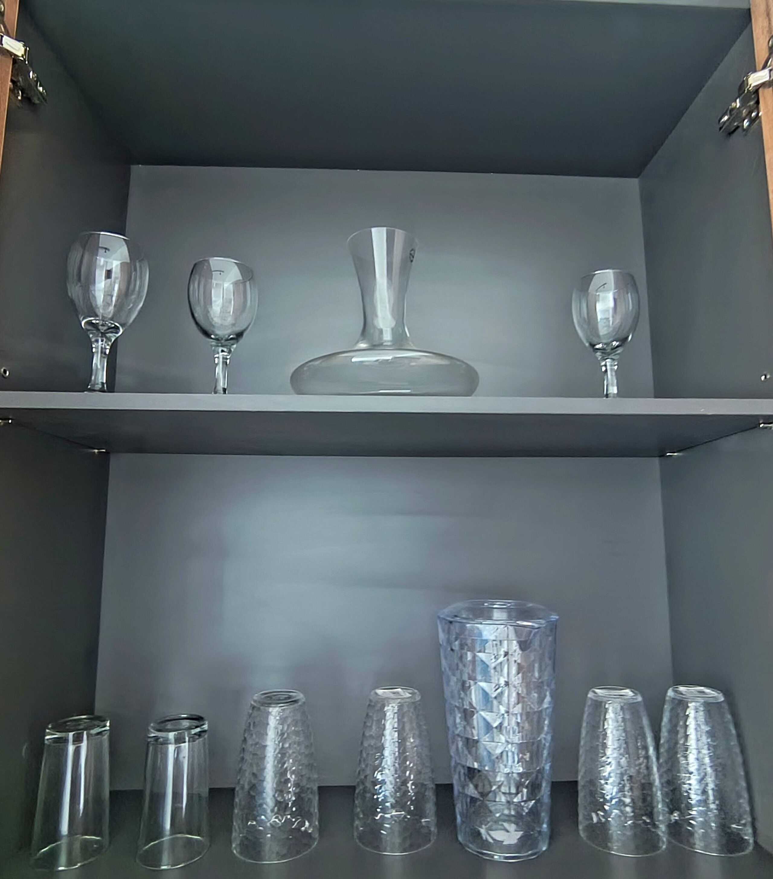 Une étagère contenant divers objets en verre, notamment des verres à vin et un vase décoratif.