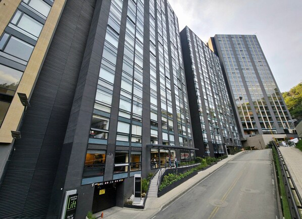 A modern high-rise building with multiple floors, large windows, and a visible entrance with a staircase leading to the ground level.