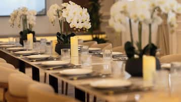 A long dining table set with white plates, clear glasses, and candles, surrounded by chairs.
